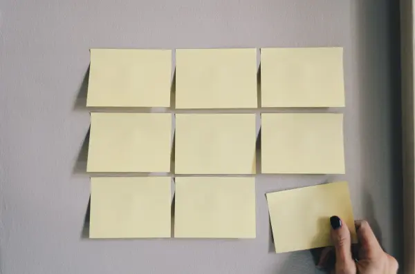 Nine sticky notes on a wall with a hand removing one, signifying the importance