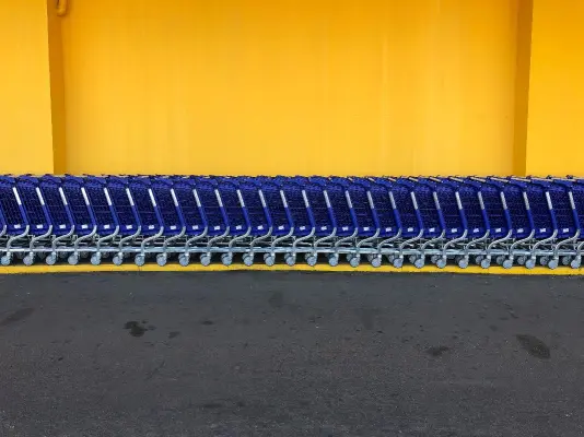 A row of blue shopping carts are lined up against a bright yellow wall