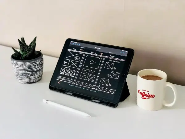 A tablet, plant, and mug of coffee sit on a desktop while a marketer strategizes