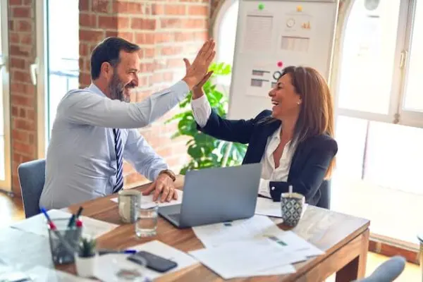 A B2B copywriter and a client high five in front of a laptop after successfully