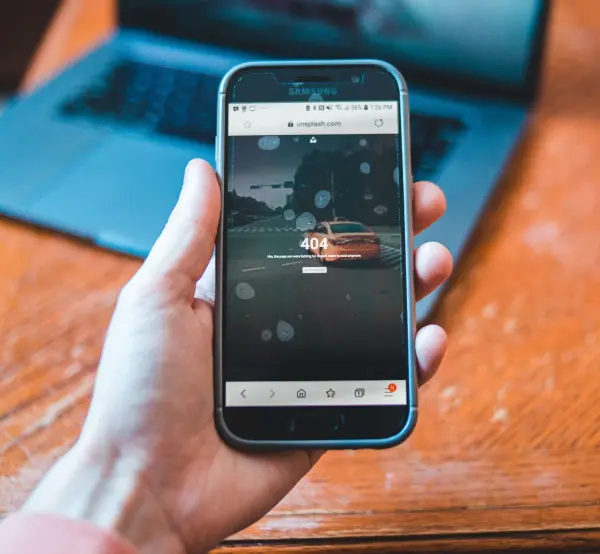 A hand holds a mobile phone with a 404 error message